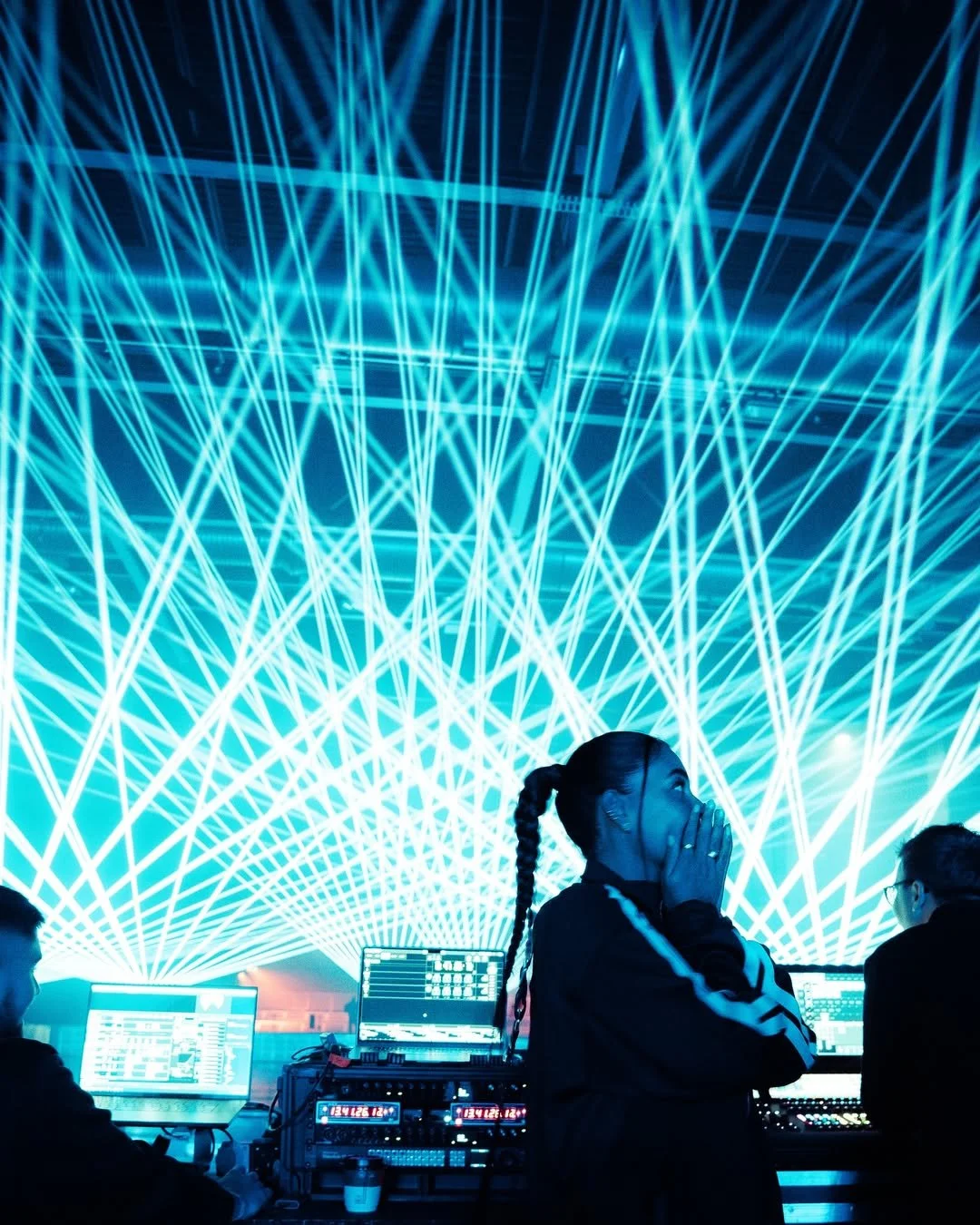 People working at a control station with laser light show overhead.