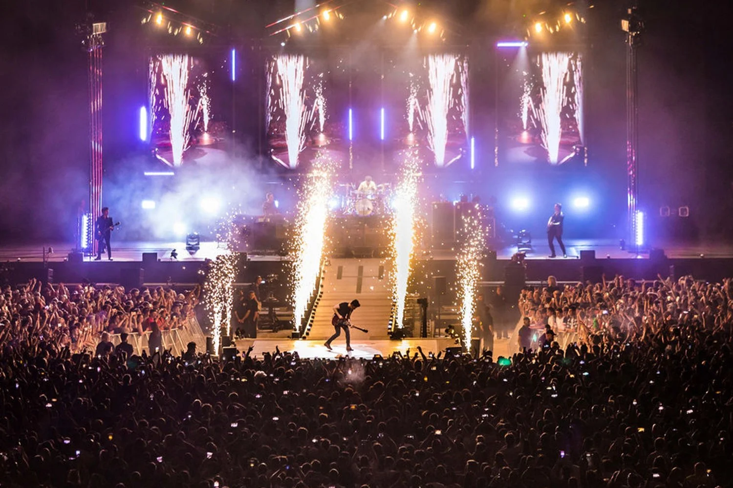 A sold-out concert with a large crowd, fireworks, and a brightly lit stage featuring a band performing live.