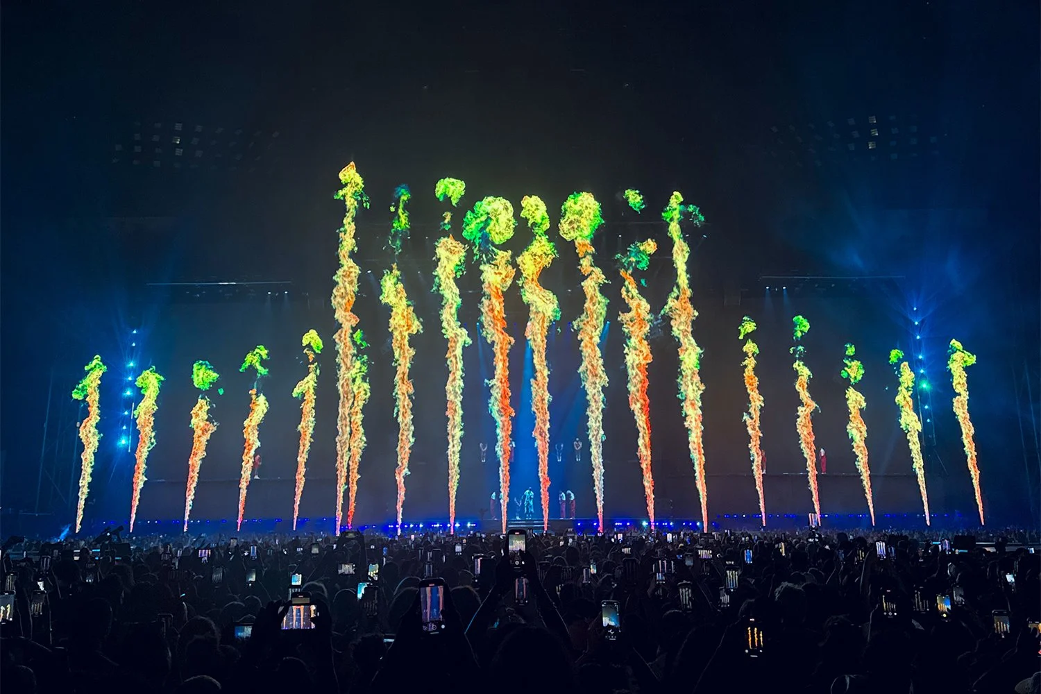 Colorful fireworks display at a concert or festival, with a crowd watching and recording on their phones.