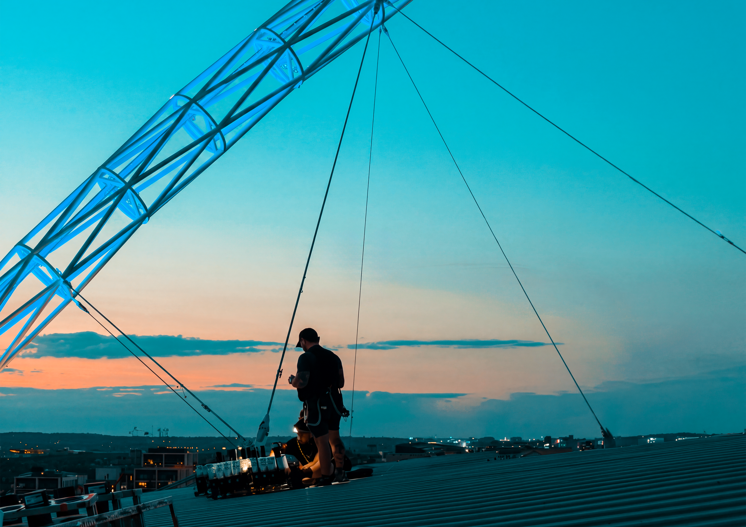 Two people working on a rooftop during sunset, with a large telecommunications tower in the background and city buildings below.