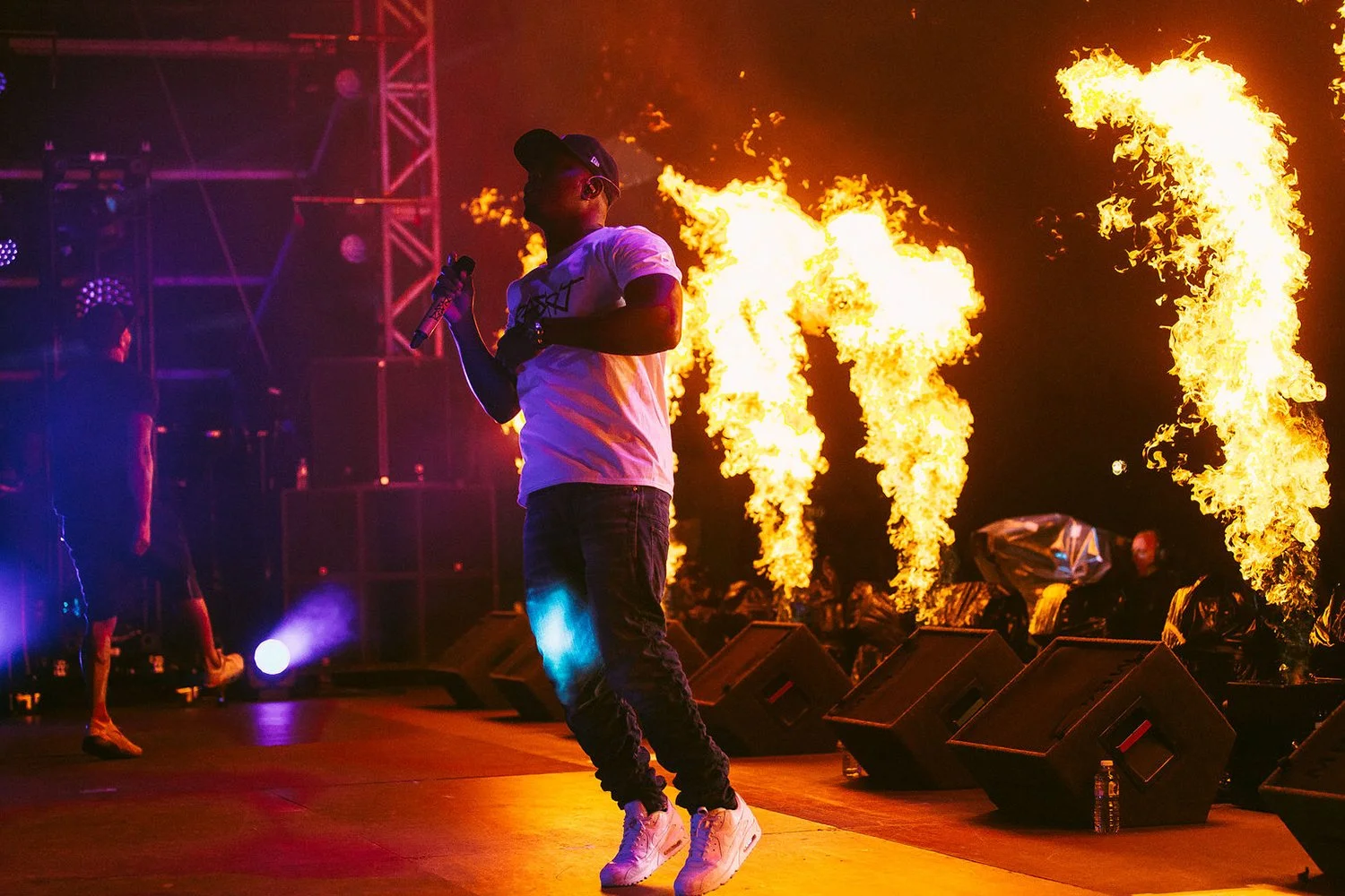 Performer on stage with flames shooting up in the background, holding a microphone