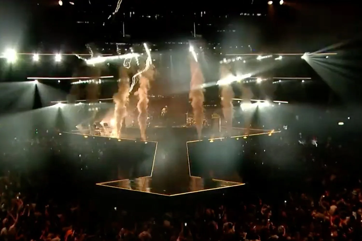 A stage with performers and fire effects in a concert or event setting, with spotlights and audience visible.