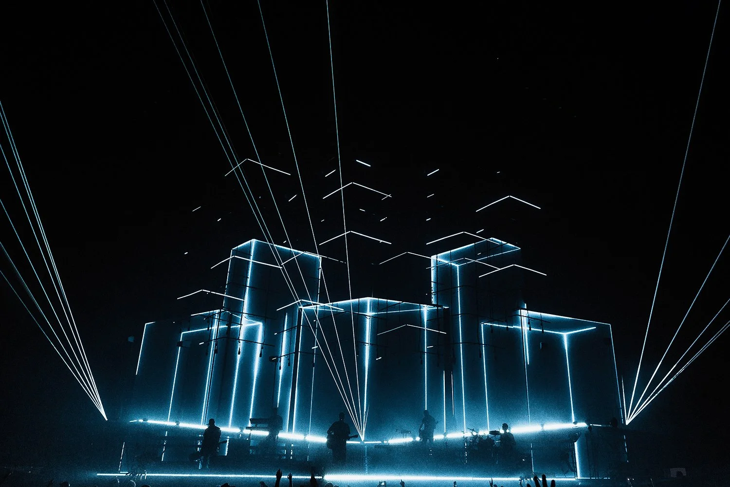 Musicians performing on stage with a futuristic LED light setup, showing illuminated geometric structures and laser beams.