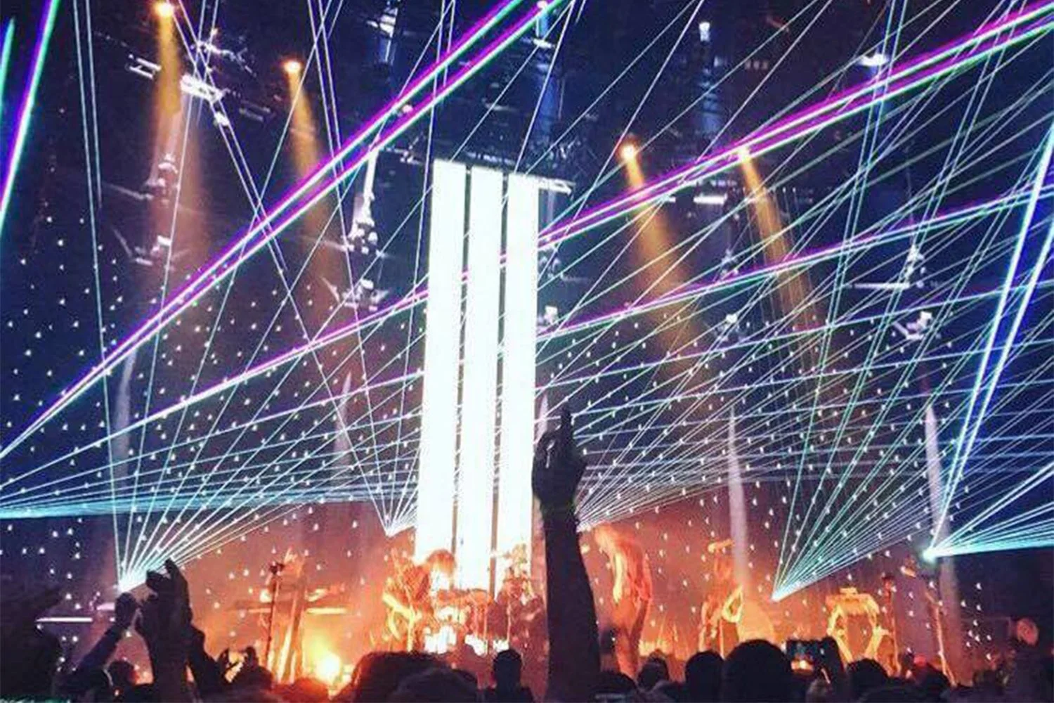 A live concert or event with a stage, colorful laser lights, and audience members raising their hands.