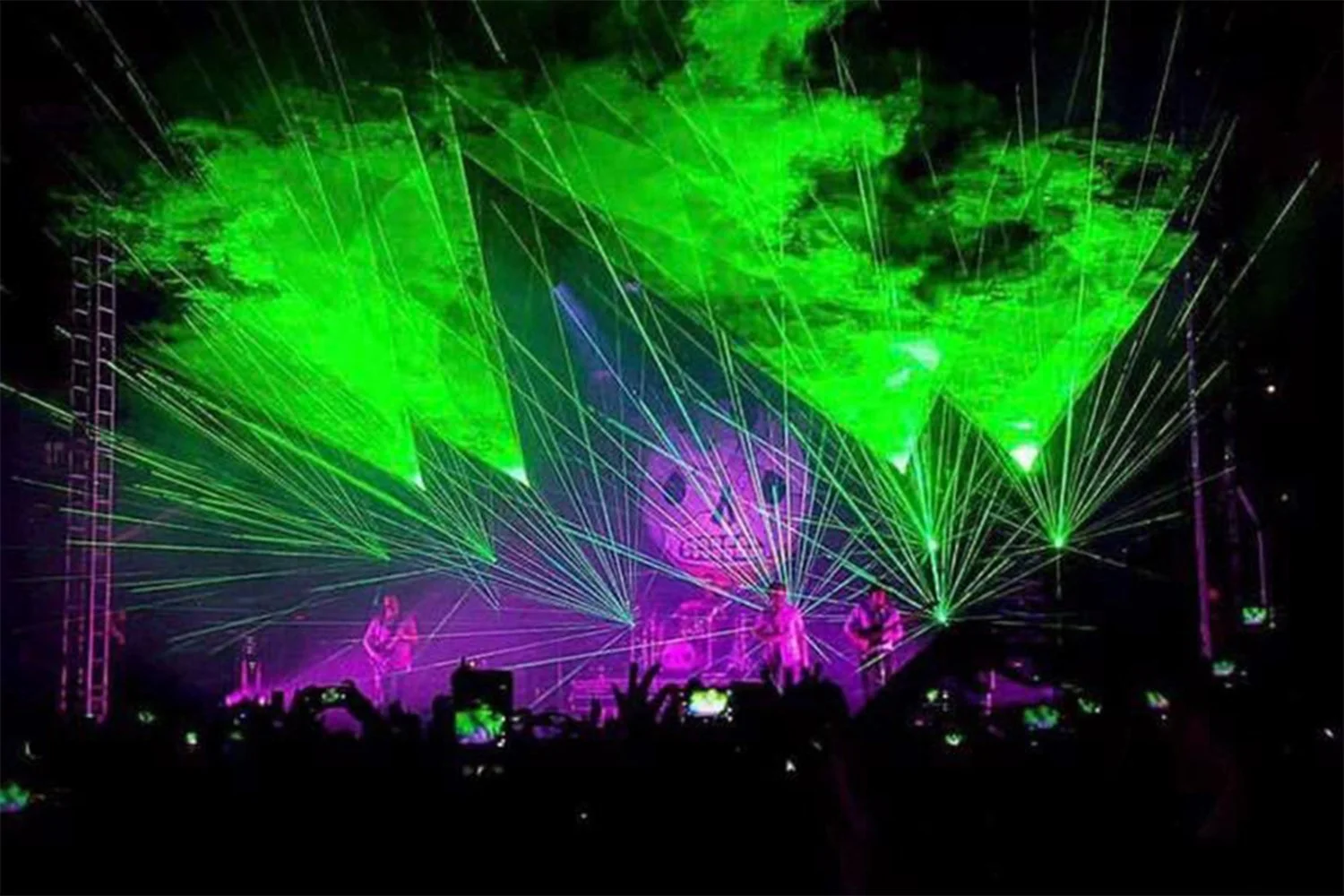 Live concert with green laser lights and a band on stage, audience taking photos.
