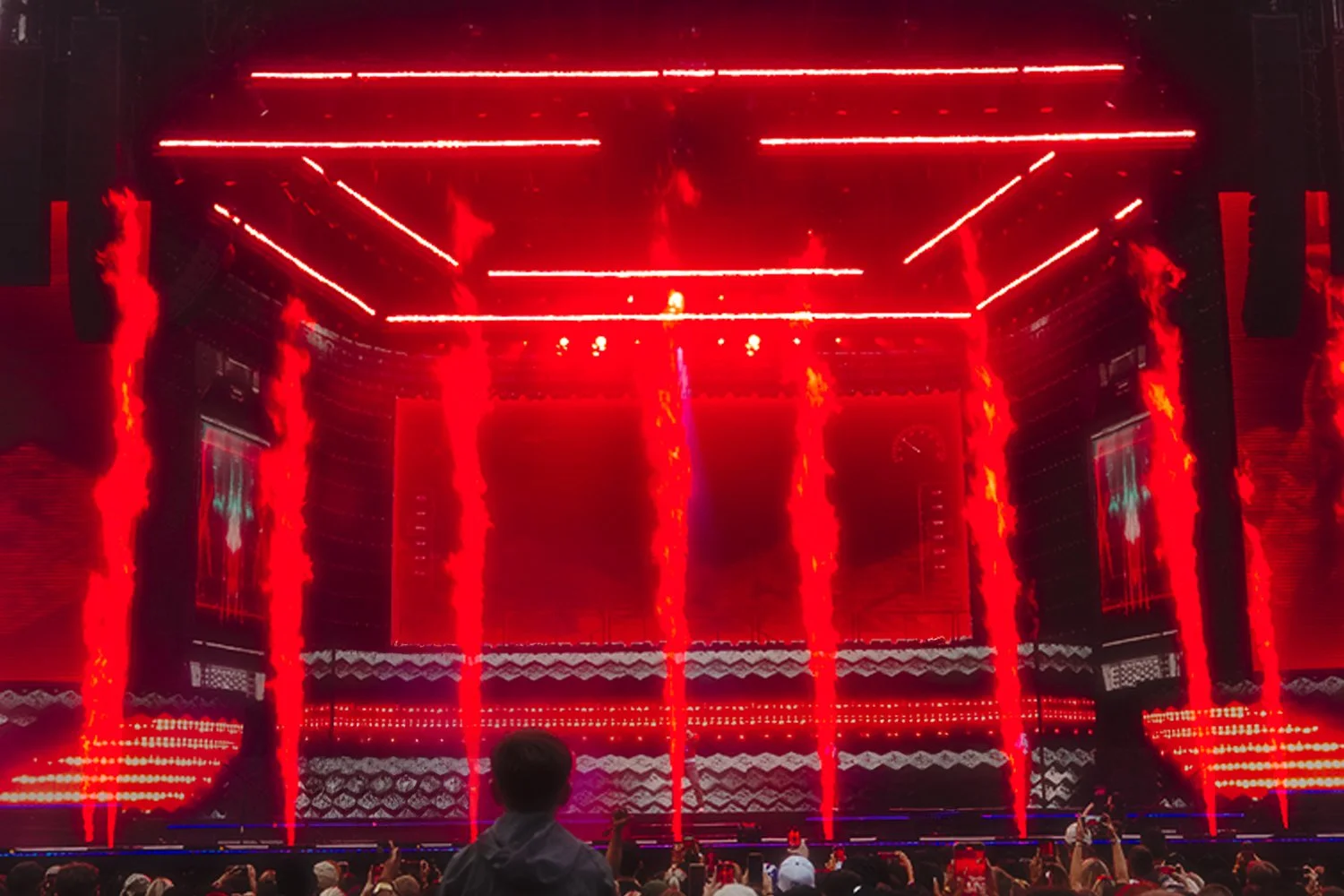 A large stage with bright red laser lights and fire effects, with silhouettes of an audience in the foreground.