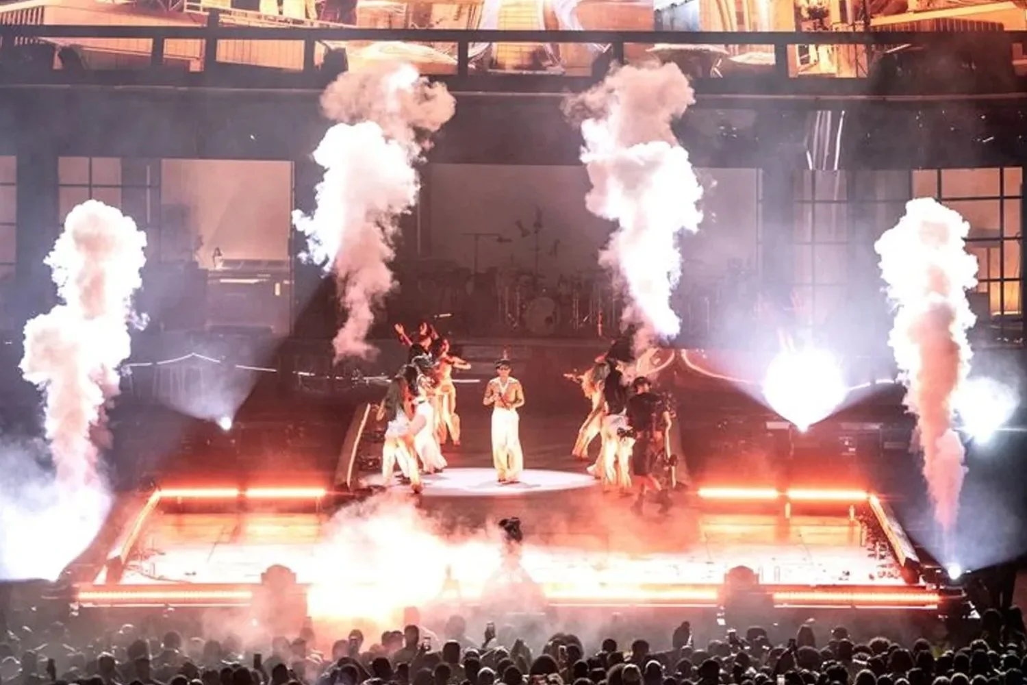 Performers on stage with smoke effects and bright lighting, audience watching in the foreground.