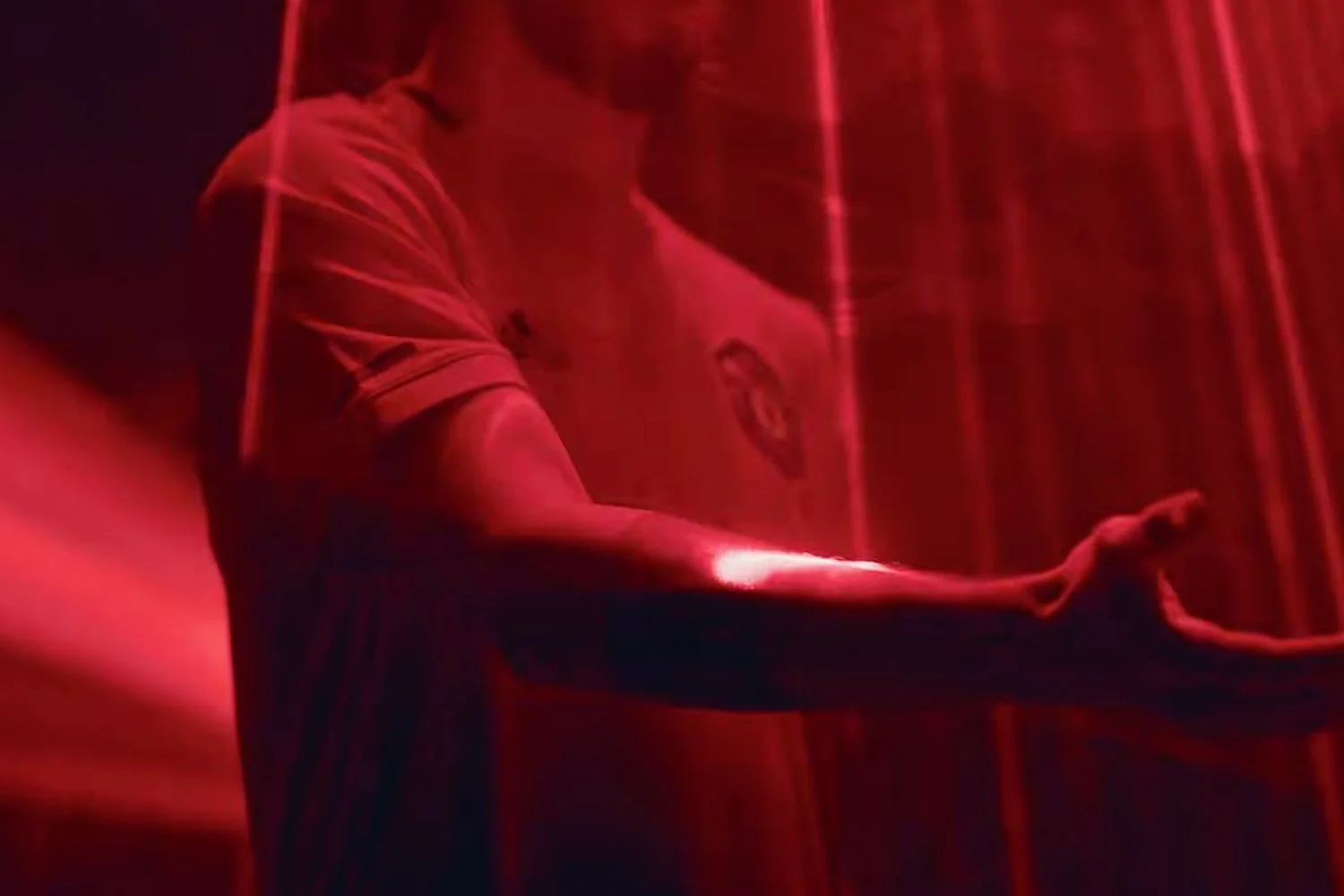 A person in a sports jersey, holding a piece of fabric, surrounded by red light and curtains, with a reflective surface on their arm.