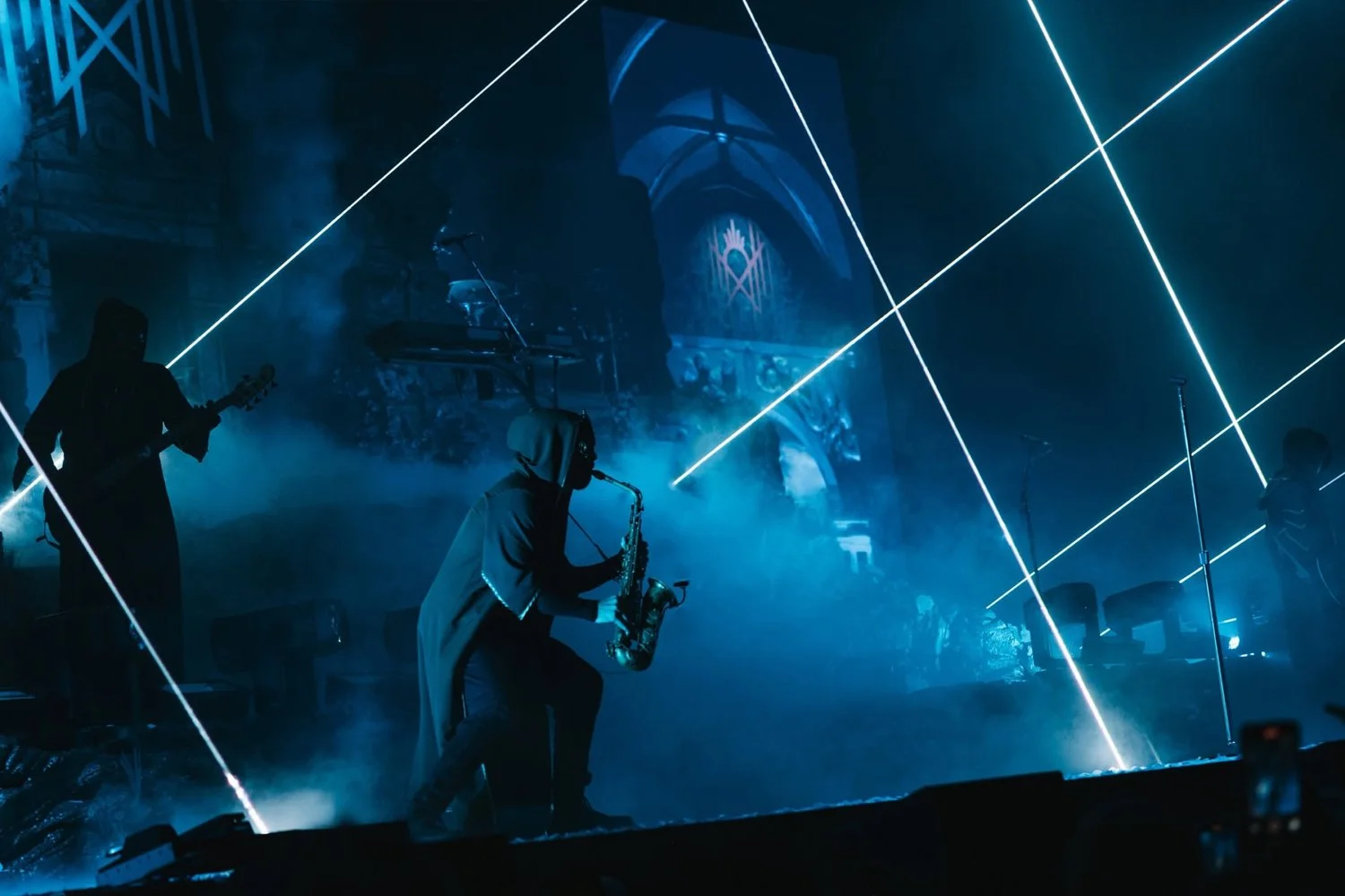 Musicians performing on a dimly lit stage with blue lighting, fog effects, and laser beams.