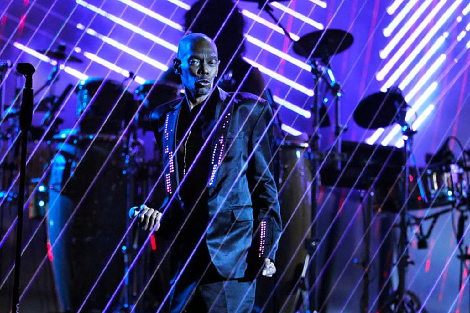 A person performing on stage with vibrant blue and purple lights and modern geometric light installations in the background.