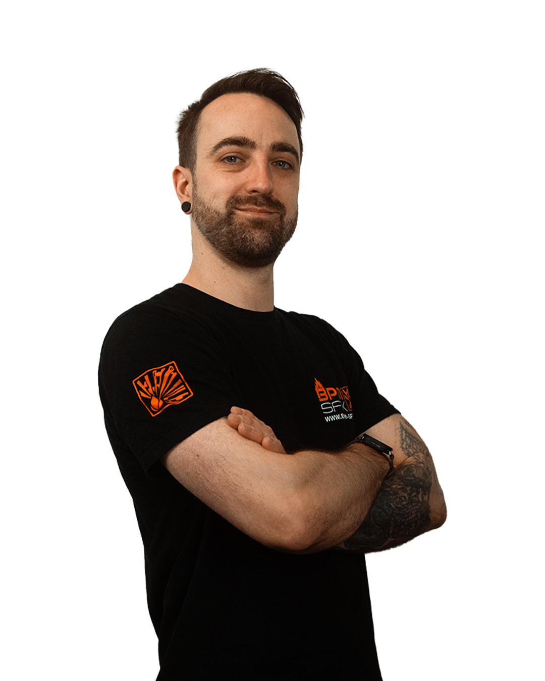 A man with a beard and tattoos on his arms, standing with his arms crossed, wearing a black T-shirt with orange graphics and logos.