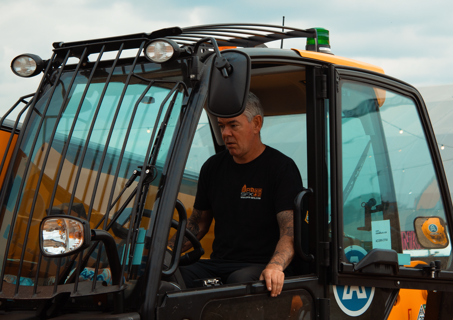 A man operating a yellow and black construction vehicle, possibly a backhoe or loader, inside the vehicle's cab.