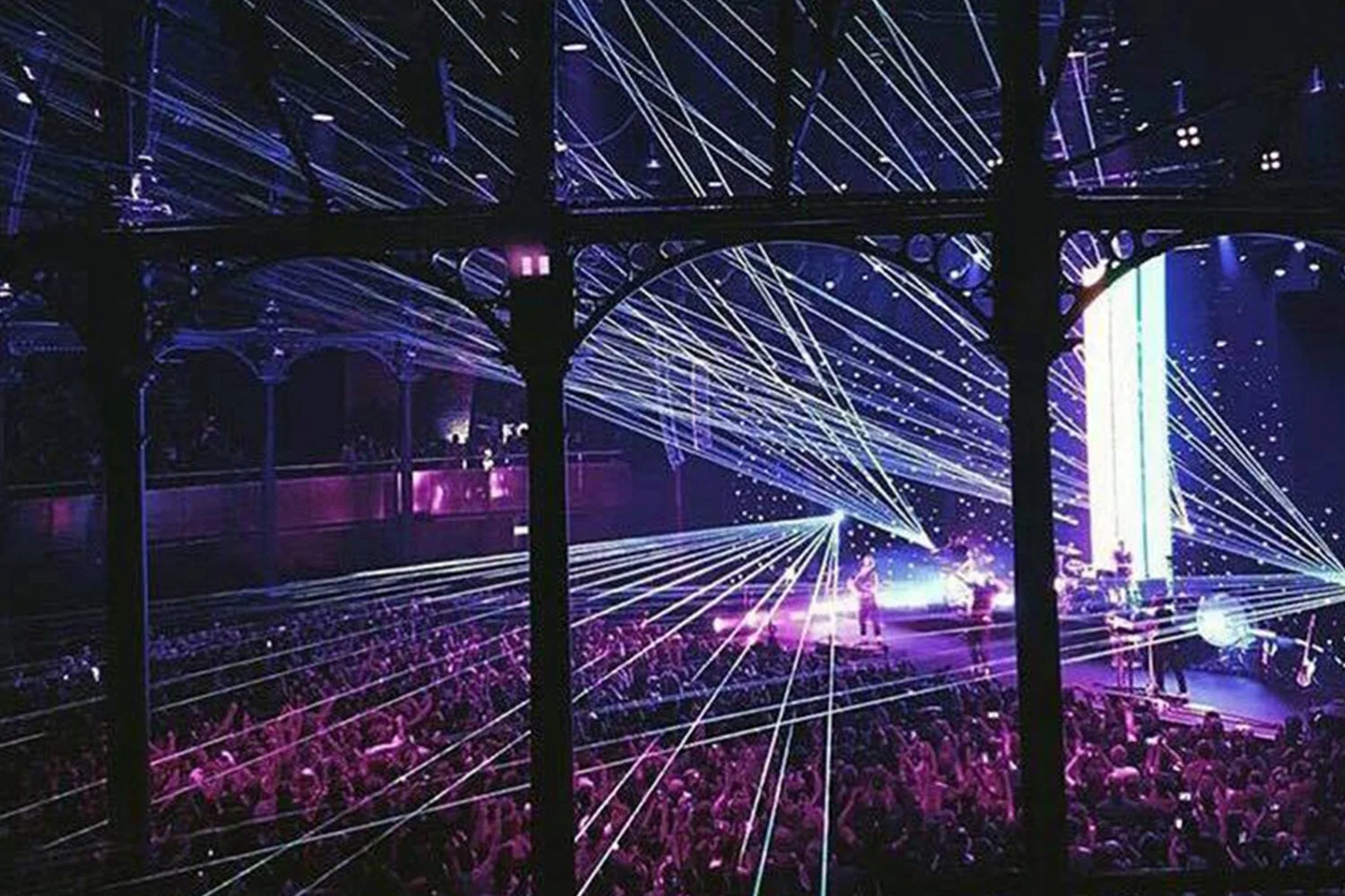 Concert or live performance with laser light show, audience, and performers on stage, with colorful light effects and laser beams.