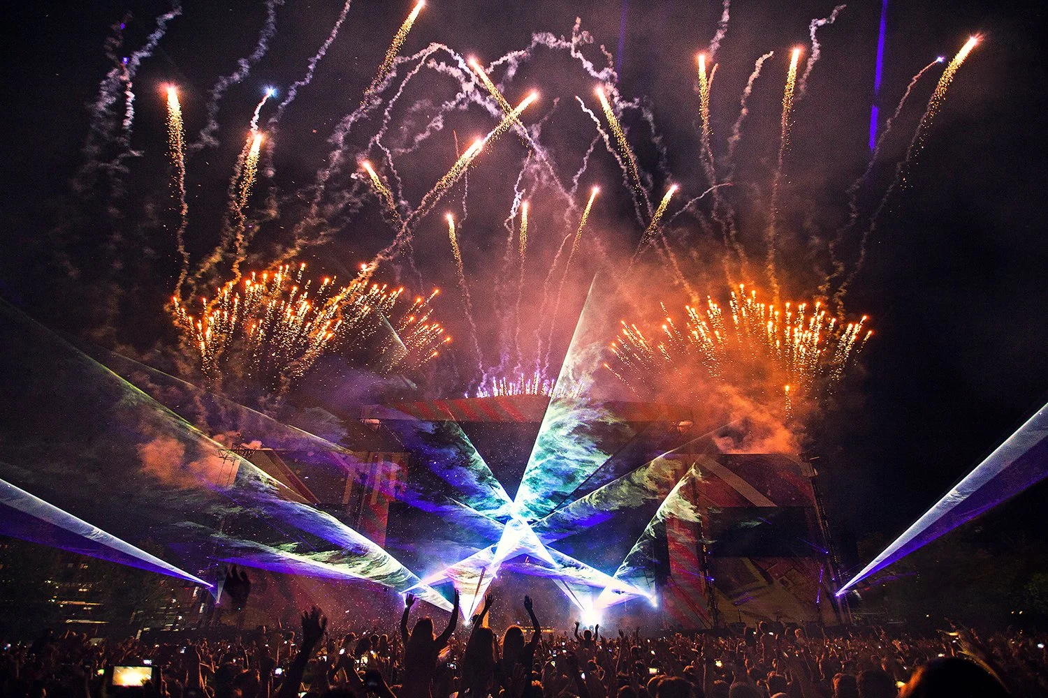 People at an outdoor concert or festival watching fireworks and laser lights during the night.