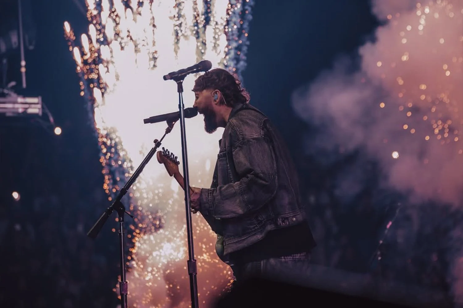 A musician performs on stage with fireworks and smoke in the background.