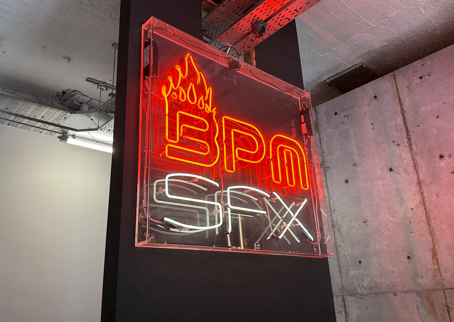 Neon sign displaying the words 'Eat', 'Drink', and 'Sexy' with a flame design at the top, mounted on a wall in an indoor setting.