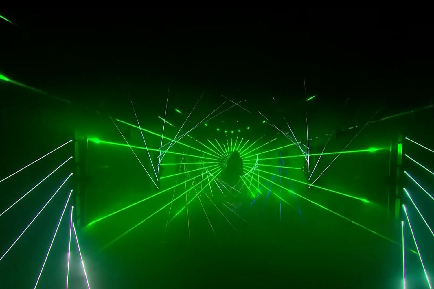 A person silhouette standing amidst green laser lights and beams creating a tunnel-like effect.