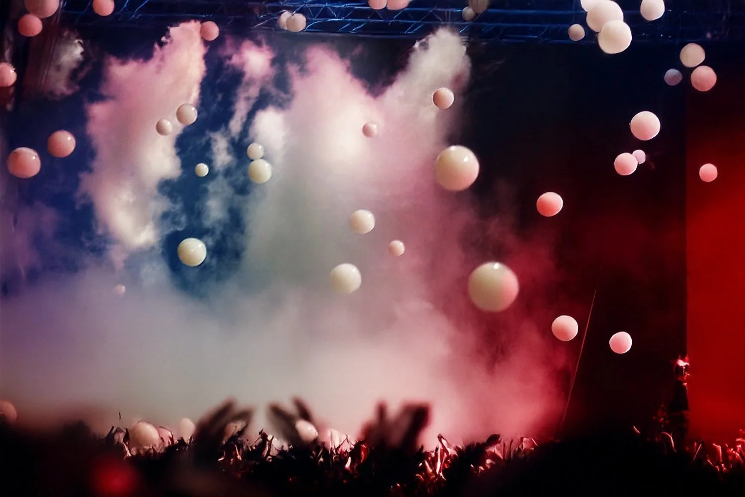 Stage with hanging white spherical balloons and colored fog, with silhouettes of audience members in the foreground.