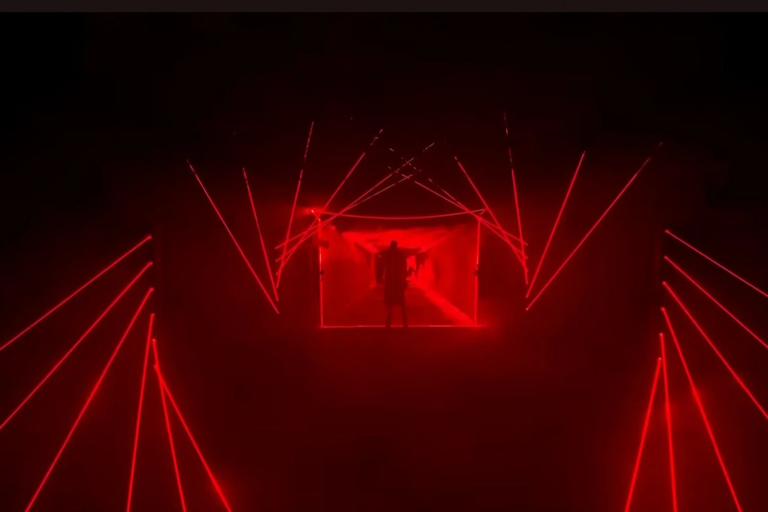 Person standing inside a tunnel of red lasers, creating a futuristic visual effect.