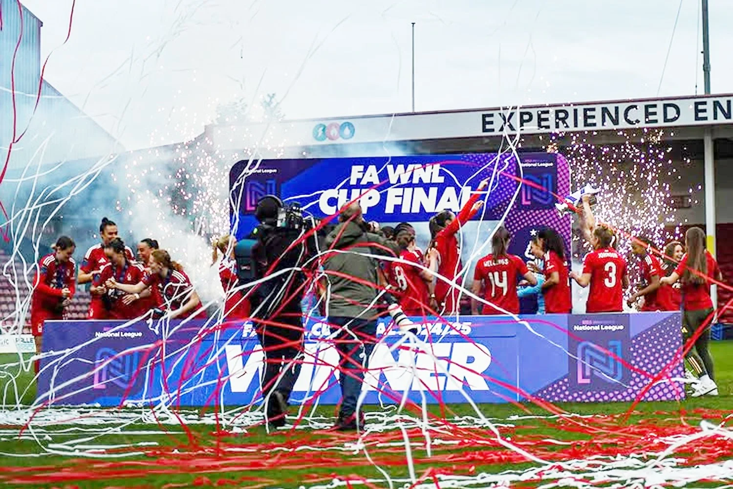Women soccer players celebrating on a field after winning a match, with confetti and streamers falling, and a banner that reads 'FA Women's Cup Final' in the background.