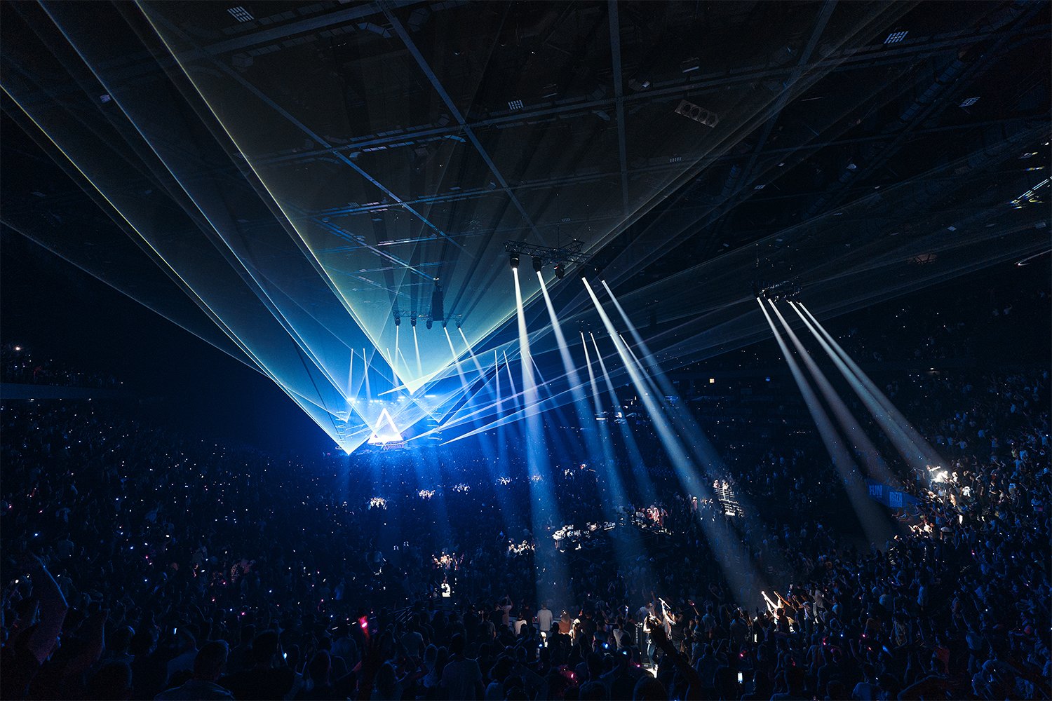 A concert or event with bright blue laser lights and an audience in a dark indoor venue.