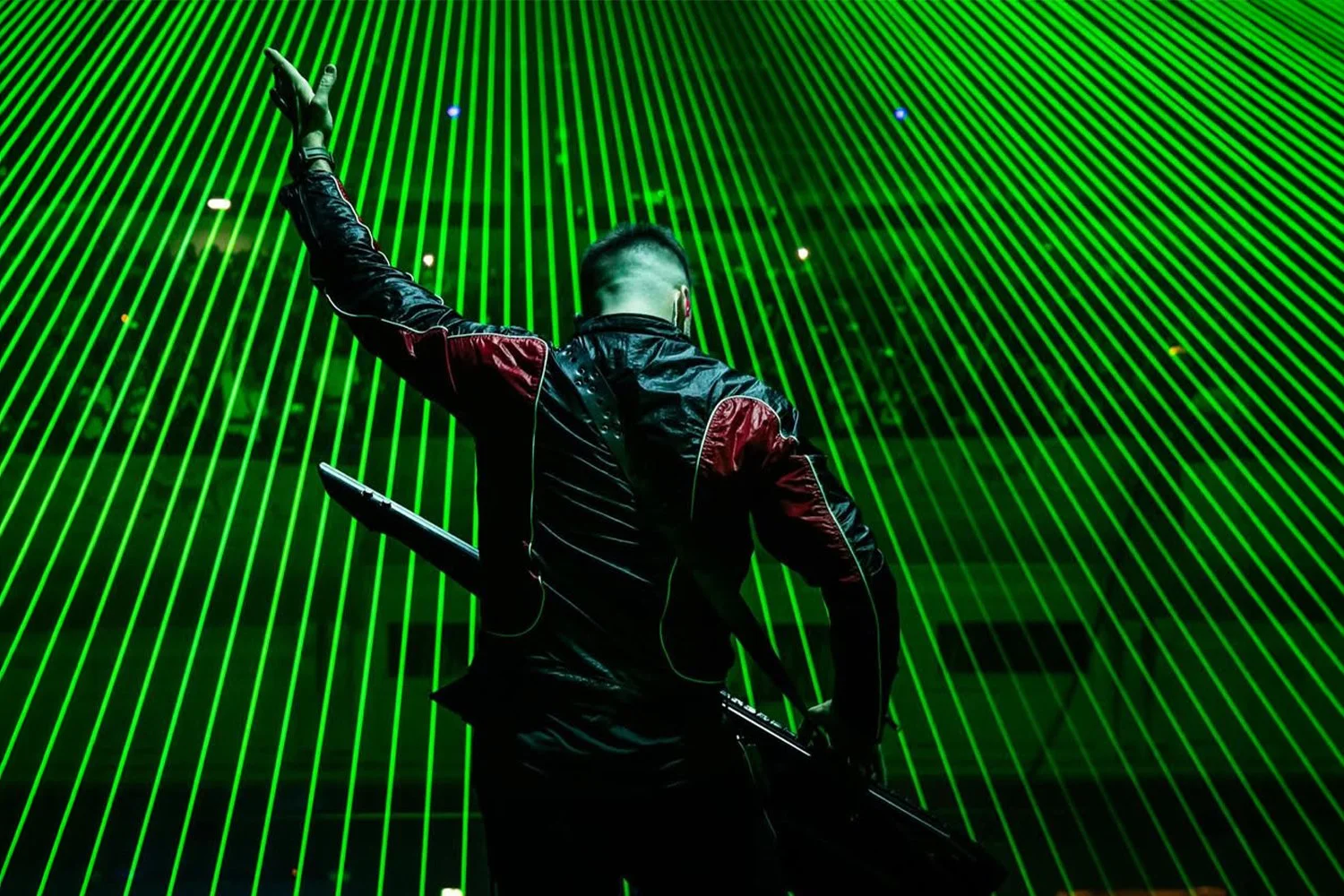 Back of a musician with a guitar in front of a green laser light display