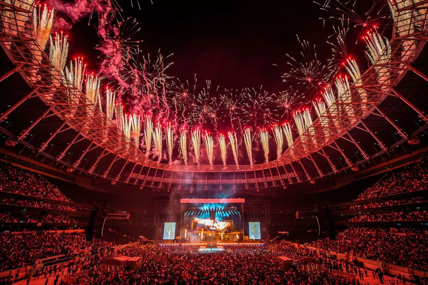Fireworks display at a concert in a large stadium with a crowd of spectators.