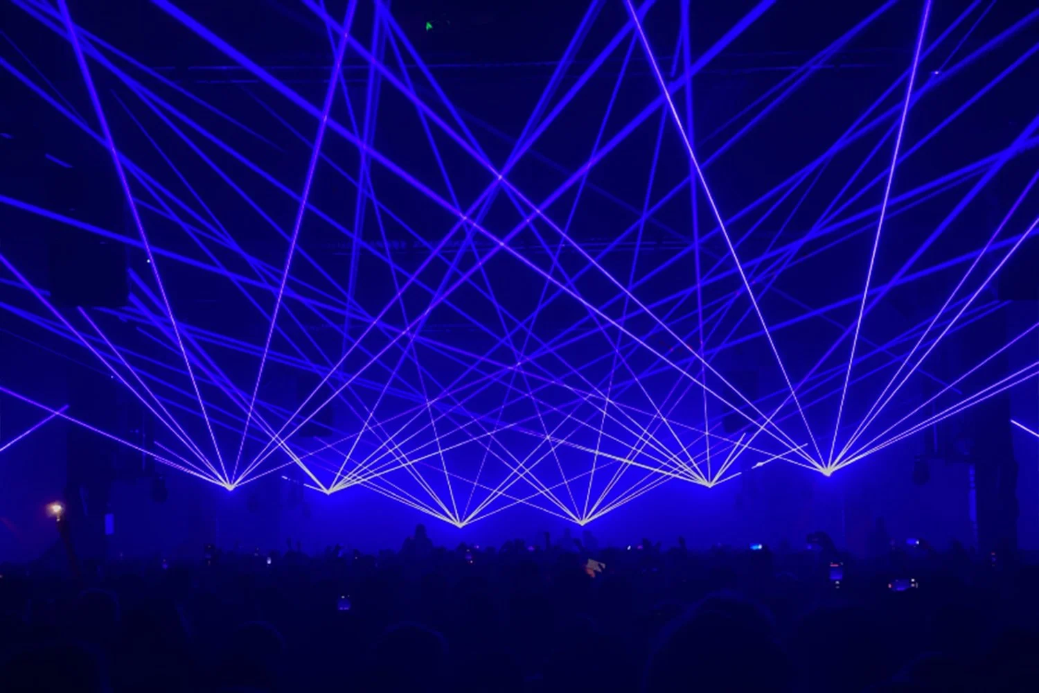 Blue laser light show with intersecting beams over a dark crowd at an event or concert.