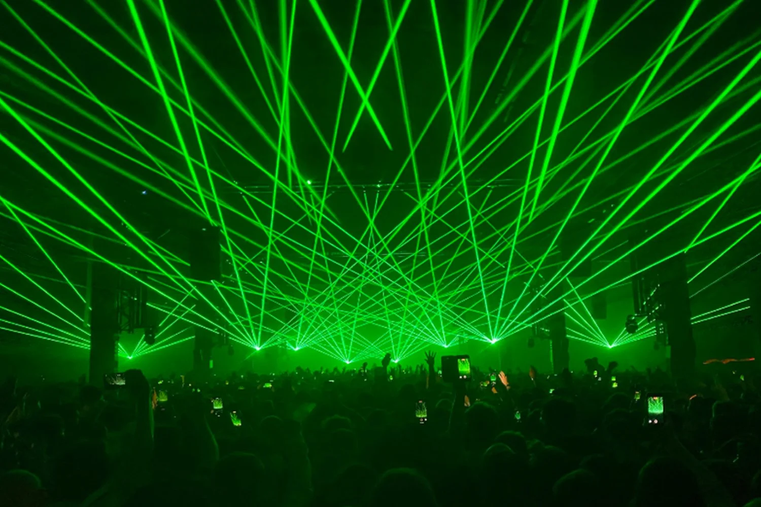 A large crowd watching a concert with green laser light show.