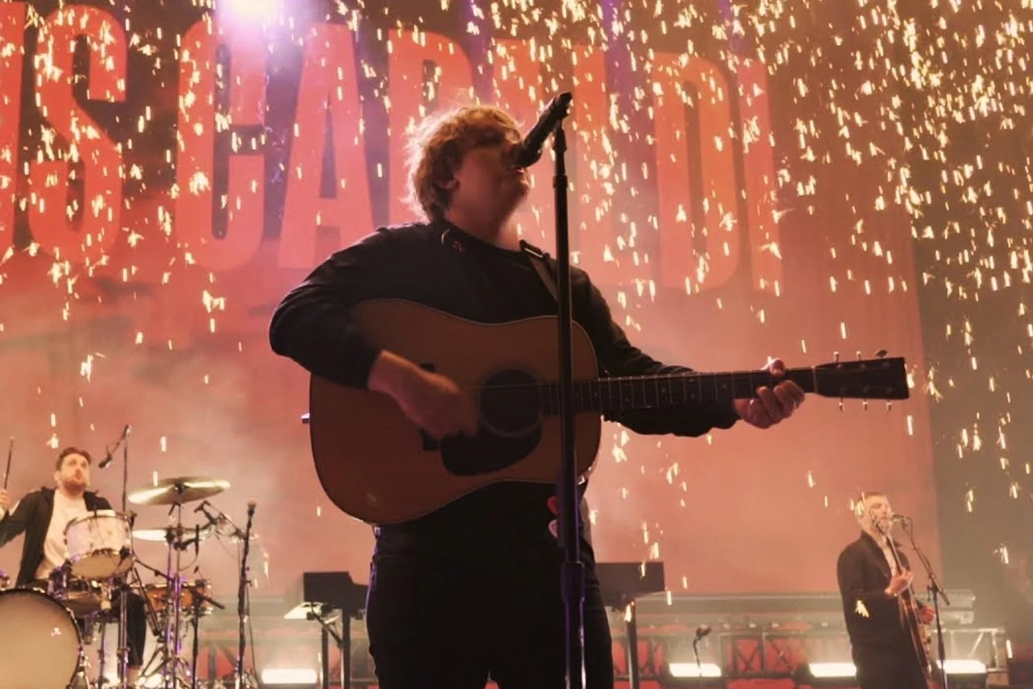 Musicians performing on stage with a backdrop of fireworks and the word 'SAVAGE' in large letters.