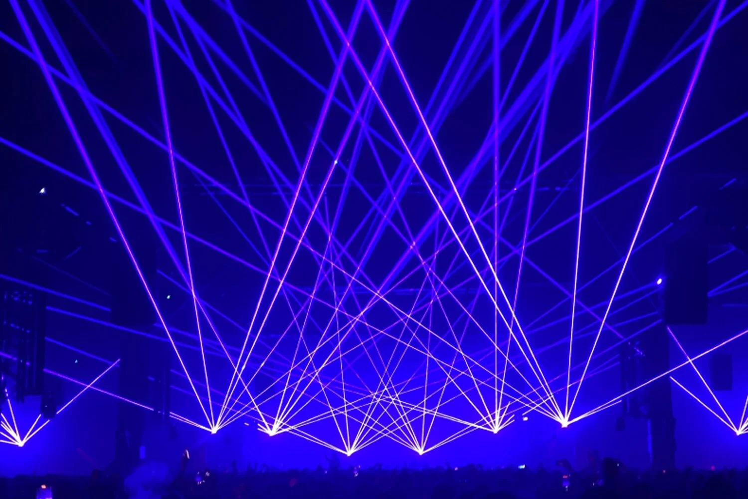 A vibrant light show with blue and purple laser beams crossing in the dark, creating a dynamic geometric pattern.
