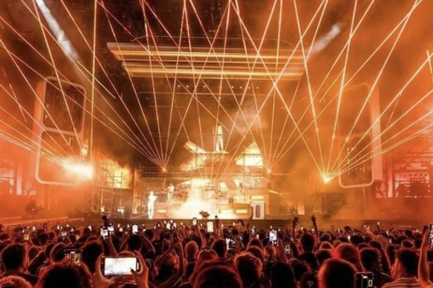 Crowd at a concert or event with laser lights and flames on stage.