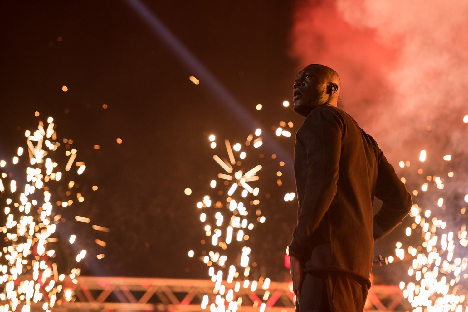 A man standing on stage surrounded by fireworks and bright sparks at night during a performance.
