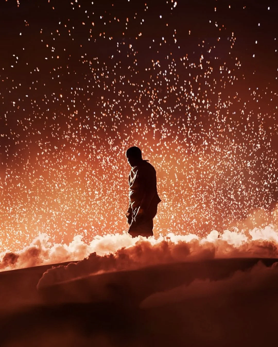 Silhouette of a young person standing on a rocky ledge with a backdrop of orange sky filled with star-like lights and clouds below.
