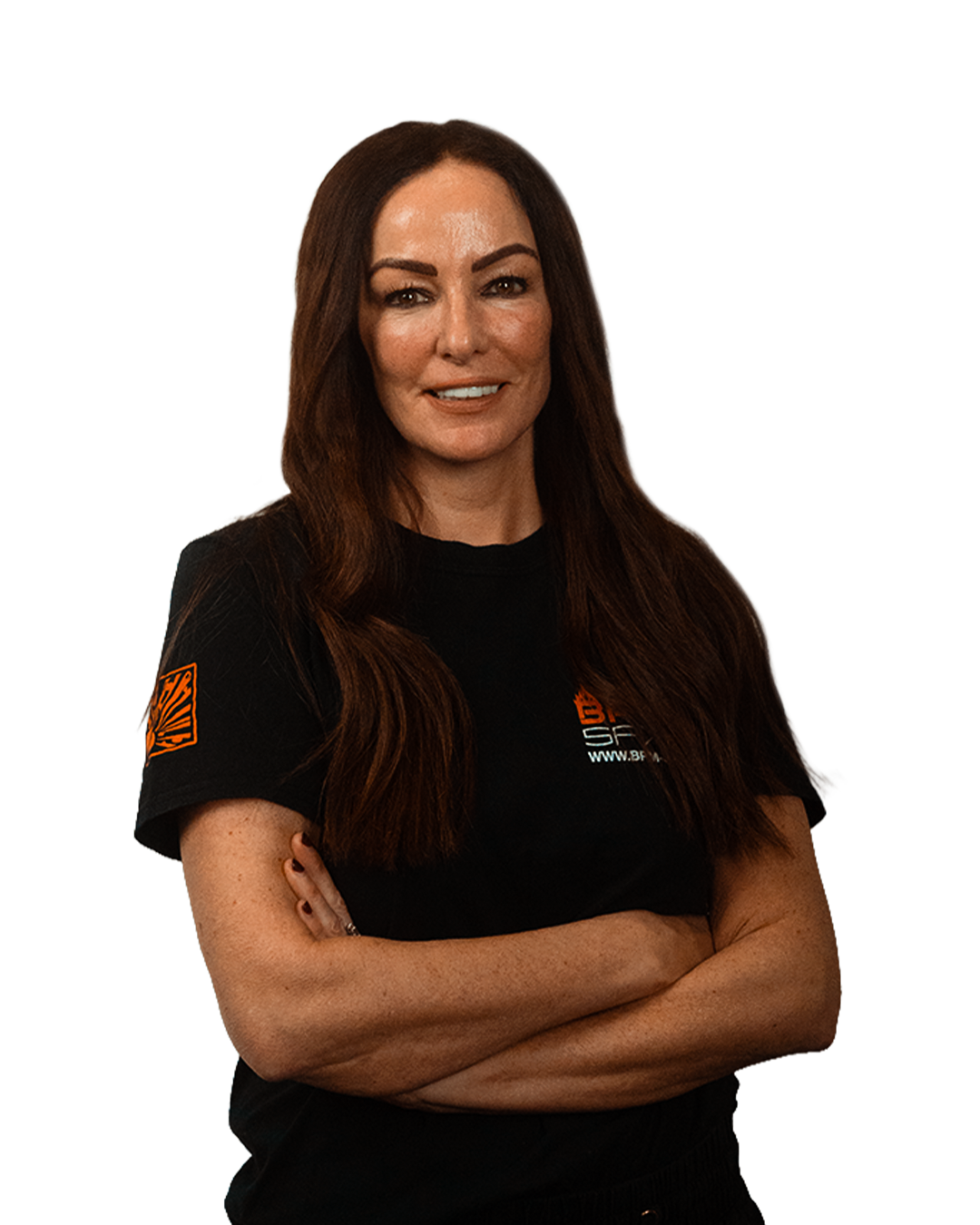 A woman with long brown hair, wearing a black t-shirt with orange and white logos, standing with arms crossed and smiling.