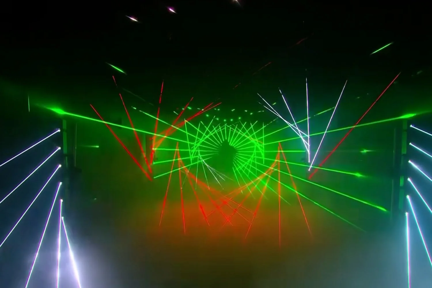Colorful laser light show with green, red, and white laser beams creating geometric patterns in the dark.