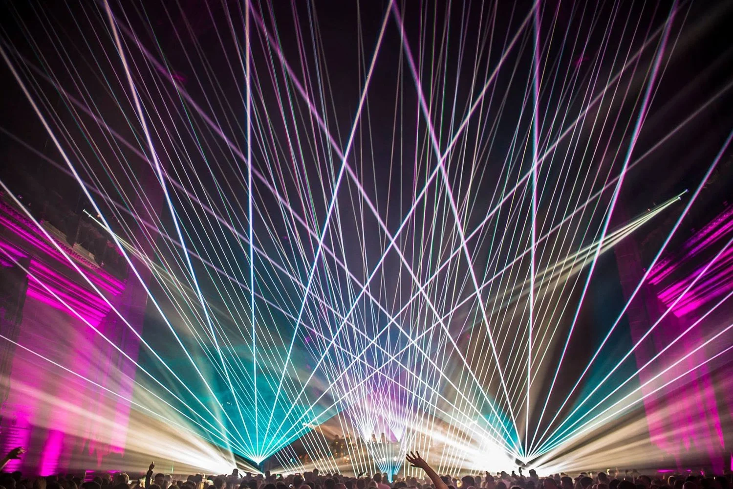 Colorful laser light show at night with a crowd of people watching.