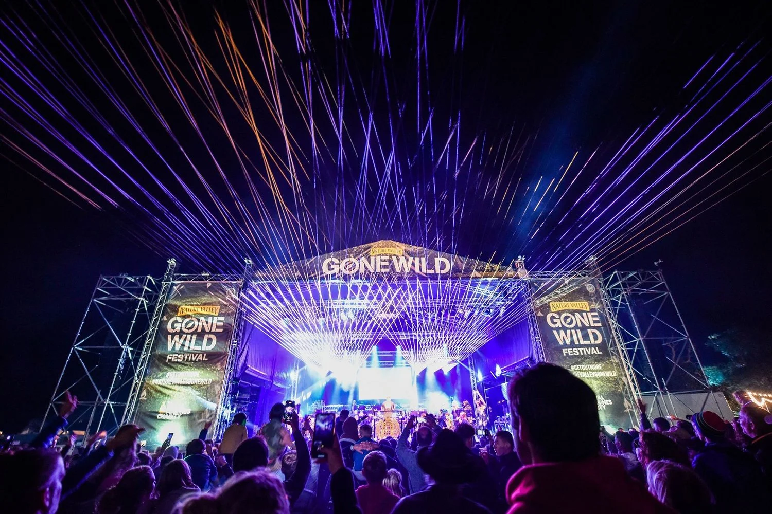 Crowd at the Gone Wild Festival with colorful light show and laser beams over stage