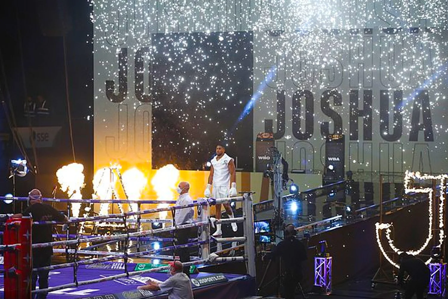 Boxing ring with fighters and referees inside, surrounded by pyrotechnics and fireworks, with a large