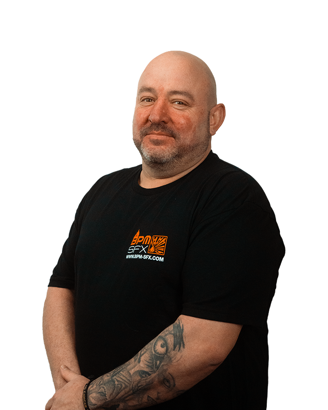 A bald man with a beard and tattoos on his left arm, wearing a black T-shirt with orange and white logo, standing against a plain background.