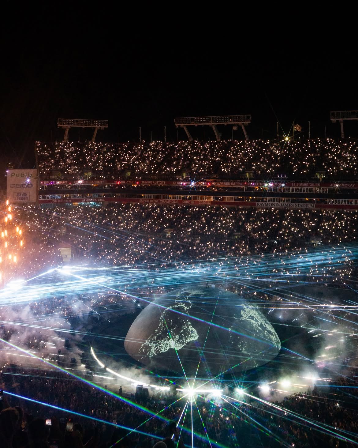 A night stadium scene with thousands of lights shining from the crowd, digital light effects, and a depiction of Earth with interconnected lines projected over the stadium floor.