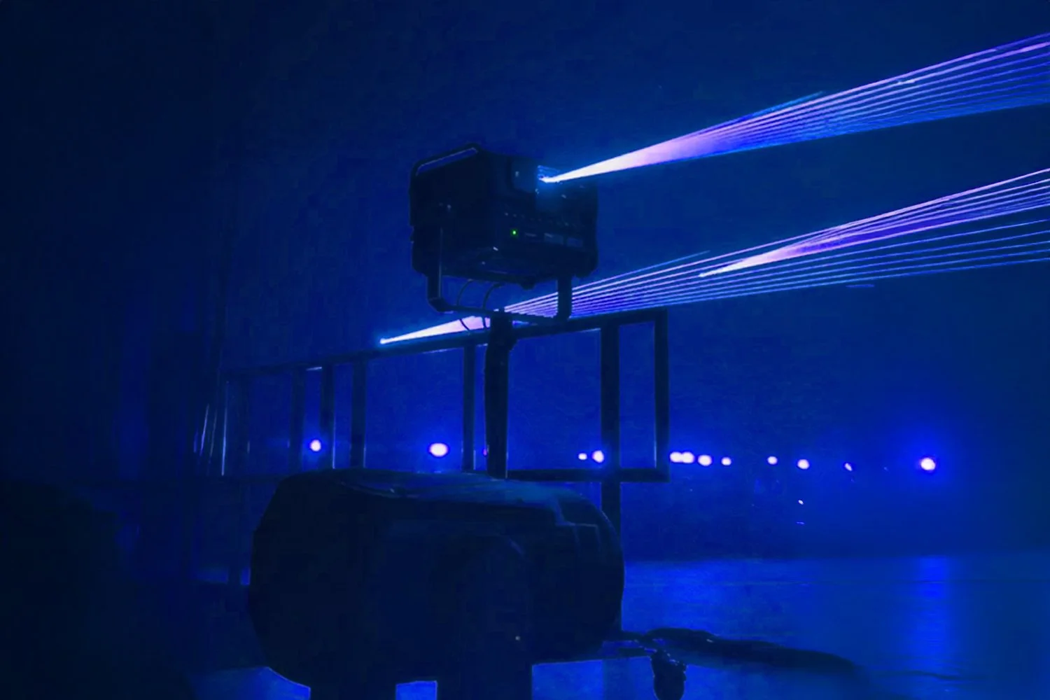 Laser light projector emitting purple laser beams in a dark room, with the device mounted on a stand and connected to a power source.