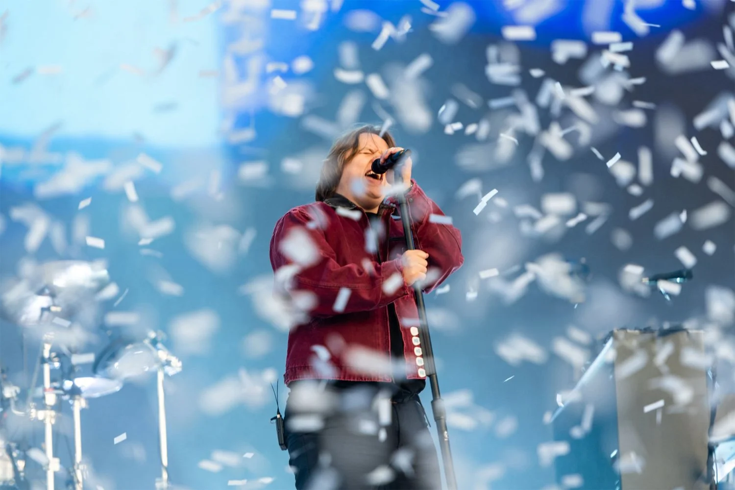 A person singing into a microphone on stage with confetti falling around them.