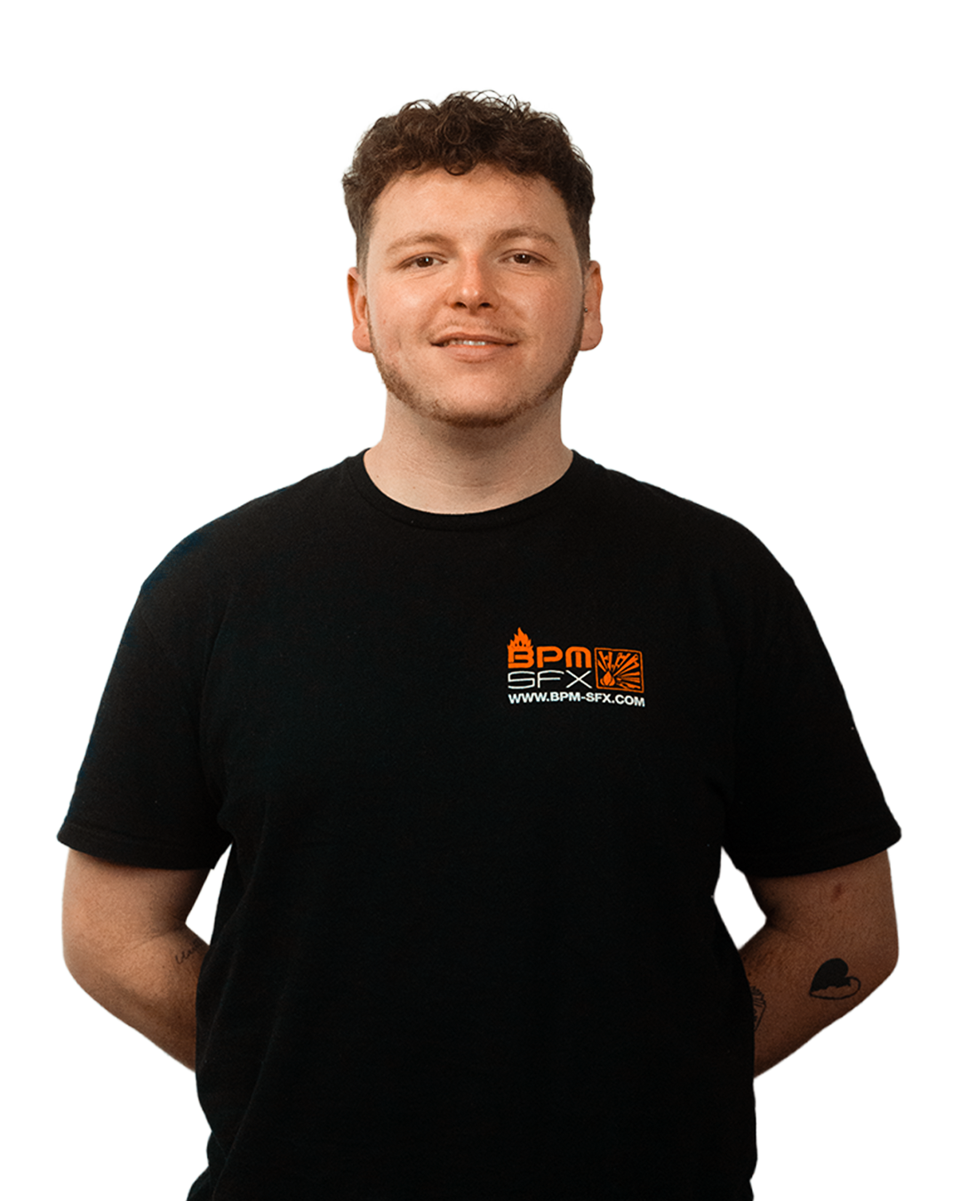 A young man with short, curly brown hair and light skin, wearing a black T-shirt with orange and white logo that reads 'BPM SFX' and a website underneath, standing with his arms behind his back.