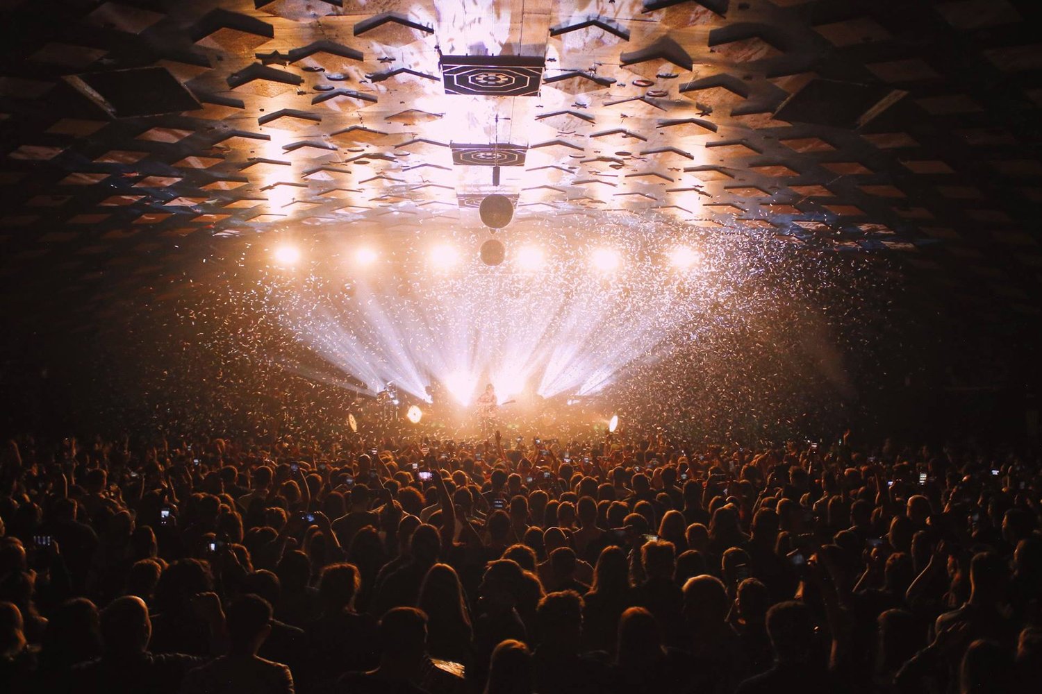 A live concert with a large audience, stage lighting, and fireworks or confetti in the air.