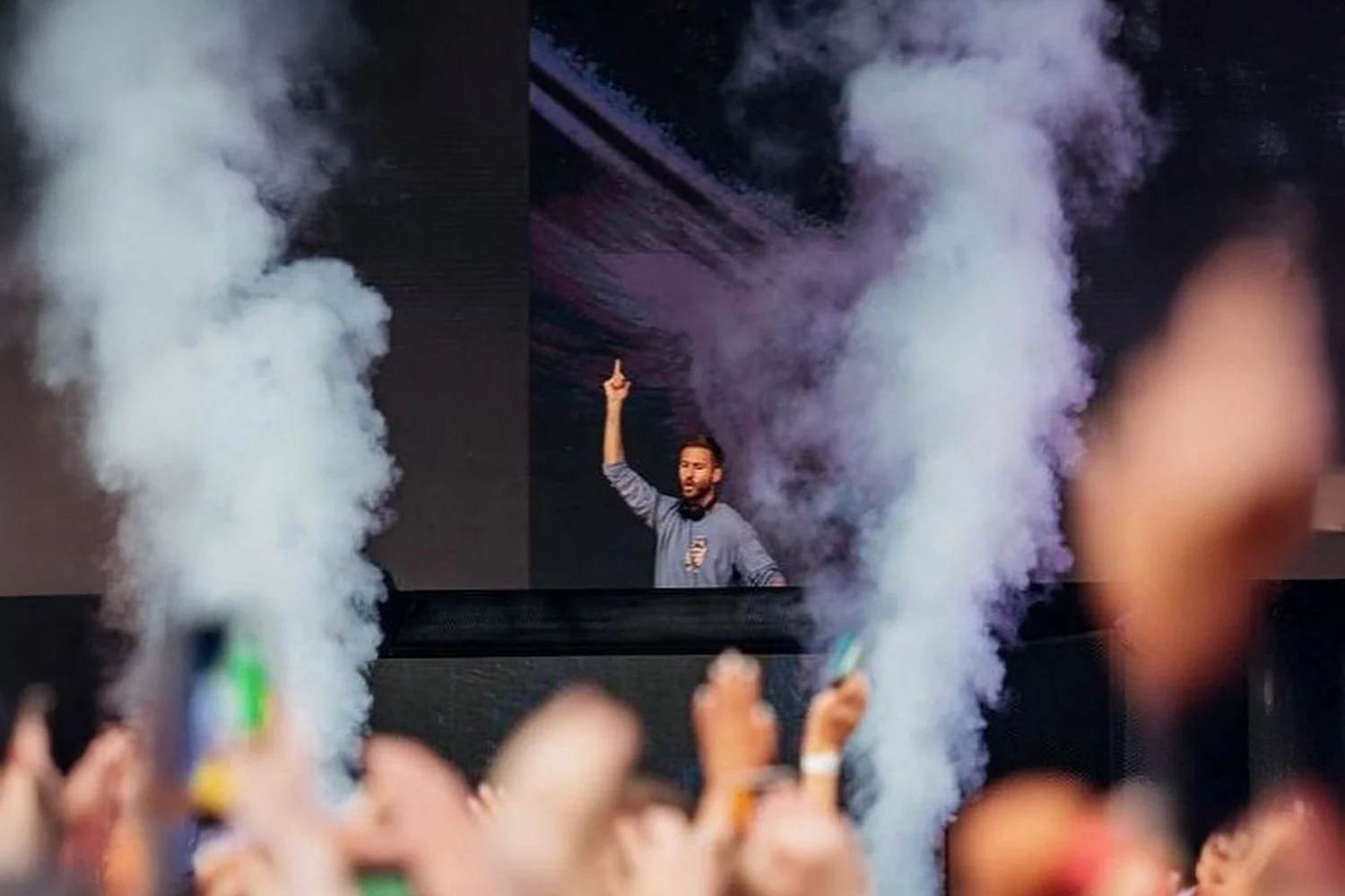A man on stage speaking or performing, with smoke effects on either side, in front of an audience.