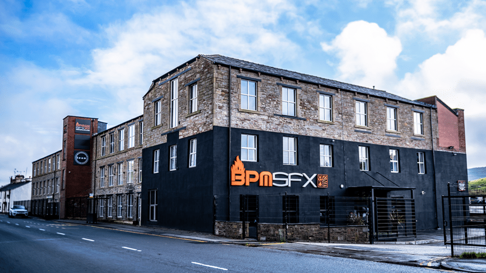 Commercial building with a black facade displaying a BPMSFX sign, upper floors made of stone bricks, and a street in the foreground.