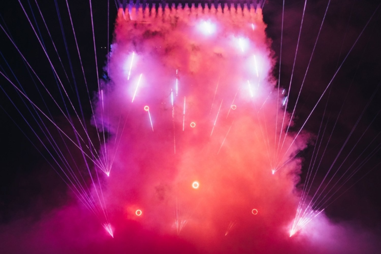 Colorful fireworks display with pink and purple hues illuminating the night sky, with streaks and circles of light.