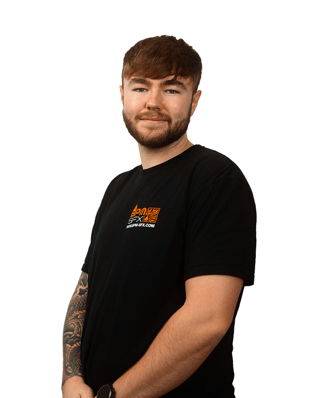 Portrait of a young man with brown hair and a beard, wearing a black t-shirt with logo, smiling softly, standing with arms crossed.