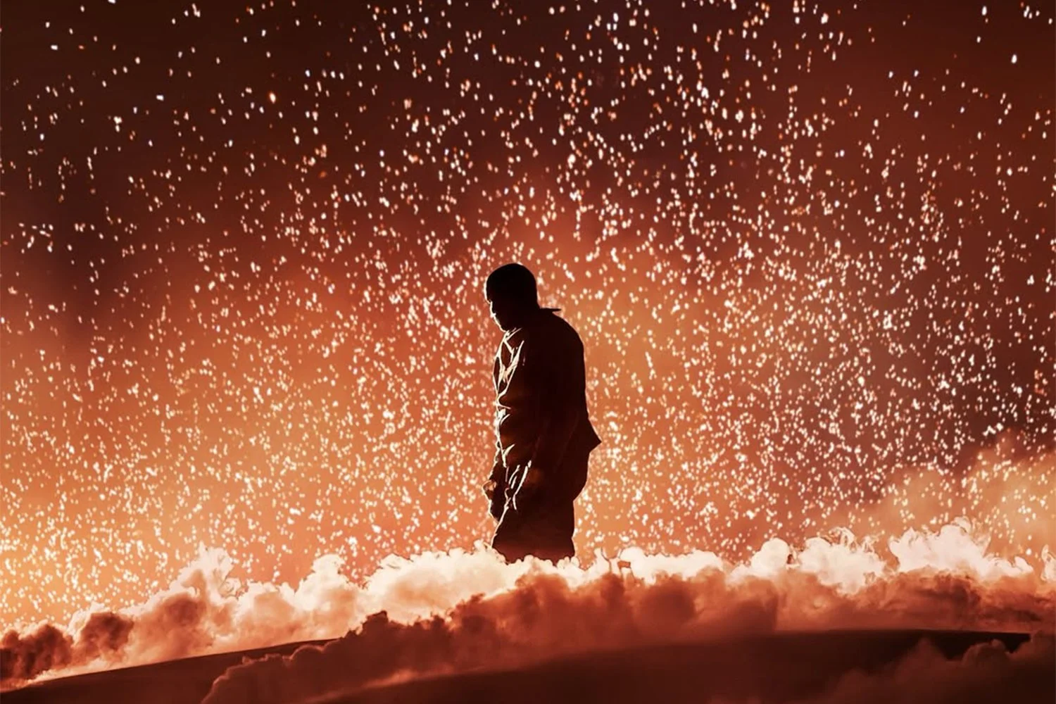 Silhouette of a man standing on clouds with a sky full of sparkling stars or fireworks in the background.